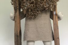 small textile figure on stilts wearing a mask made of agapanthus seed heads