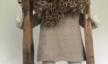 small textile figure on stilts wearing a mask made of agapanthus seed heads