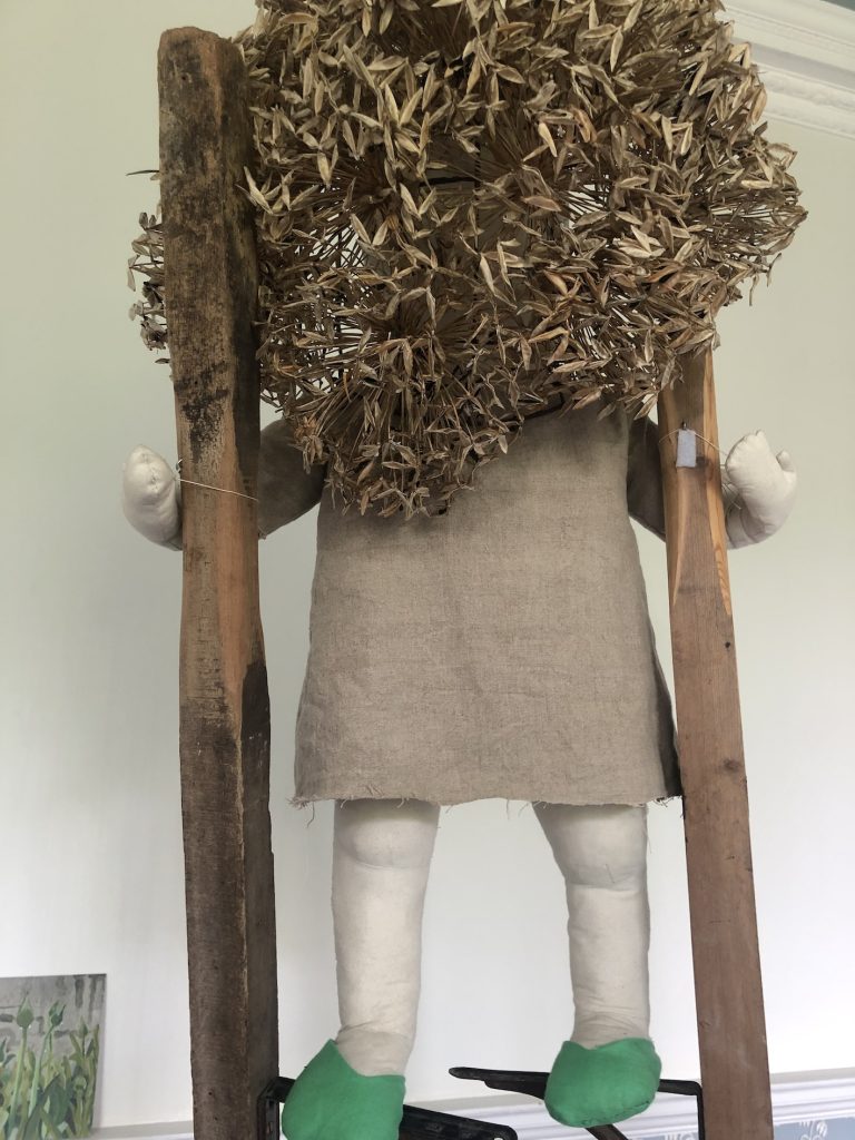 small textile figure on stilts wearing a mask made of agapanthus seed heads